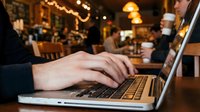 Young man typing on laptop in cozy coffee shop, remote work and freelance lifestyle concept with warm bokeh lights in background.