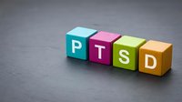 Colorful wooden blocks spelling PTSD on gray surface, representing post-traumatic stress disorder awareness and mental health education.