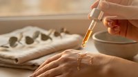 Natural skincare routine with dropper bottle applying serum to hand in warm sunlight creating peaceful wellness atmosphere for beauty treatments.