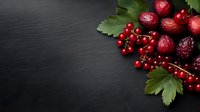 Fresh red berries and strawberries with green leaves arranged on dark slate background for culinary and healthy eating concepts.