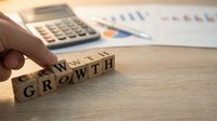 Wooden blocks spelling GROWTH on desk with calculator and financial charts in background for business planning and development concepts.