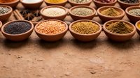 Assorted colorful spices and grains displayed in wooden bowls on rustic surface for cooking, seasoning and culinary preparation in kitchen or market setting.