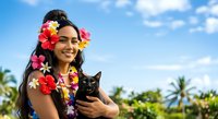 Young woman of South Asian descent wearing colorful flower lei garlands holding black cat outdoors in tropical setting with palm trees and blue sky, suitable for travel, lifestyle, and pet-related content.