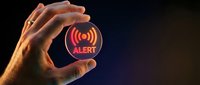 Hand holding glowing red alert notification icon with wireless signal waves on dark background, representing emergency warning, cybersecurity threat, or system notification alert.