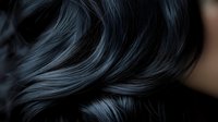 Luxurious dark wavy hair close-up showing silky smooth texture and natural shine against black background. Professional haircare and beauty concept.