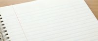 Open spiral notebook with blank lined pages on wooden desk surface ready for writing notes or journaling.