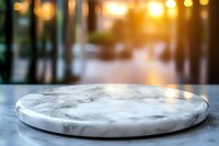 Empty round marble plate on gray surface with blurred warm bokeh background, natural sunlight creating atmospheric mood for food photography and product display.