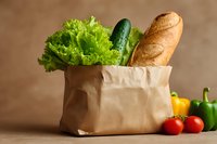 Paper grocery bag filled with fresh vegetables and bread on wooden table for healthy cooking and meal preparation.