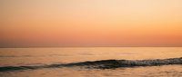 Serene ocean waves at golden hour with warm orange and pink sunset sky reflecting on calm water surface creating peaceful seascape atmosphere.
