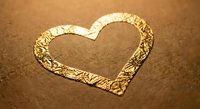 Heart shape drawn in golden sand on beach surface with textured edges and warm lighting for romantic designs and love concepts.