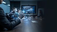 Businessman in dark suit analyzing digital financial data with holographic charts and graphs displayed on transparent screen in modern office conference room setting.