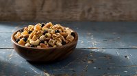 Wooden bowl filled with mixed nuts and dried fruits on rustic blue wooden table. Healthy snacking, organic food ingredients for cooking and baking.