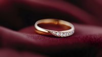 Golden engagement ring with small diamonds on red velvet background, elegant jewelry photography showing fine craftsmanship and luxury details.