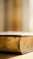 Vintage aged book with worn golden pages and weathered binding on wooden surface with soft warm lighting creating nostalgic atmosphere for literary projects.