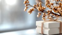 White gift box with rustic twine bow near dried cotton branches against soft blurred background, creating minimalist festive composition for holiday season.
