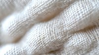 Close-up macro view of white cotton fabric texture showing detailed weave pattern and soft textile fibers in natural light, creating abstract background pattern.