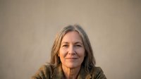 Mature woman with long gray hair and olive complexion wearing olive-colored top against neutral beige background, suitable for healthcare, wellness, lifestyle, and professional portrait use.