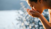Young woman drinking fresh clean water from cupped hands outdoors in natural sunlight. Hydration and healthy lifestyle concept for wellness campaigns.