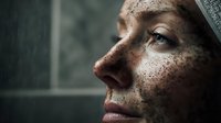 Close up profile portrait of young woman with natural freckles looking up through window light, dramatic moody atmosphere with soft shadows and natural skin texture.