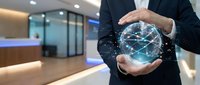 Businessman holding glowing digital network sphere with connected nodes in modern office environment representing global connectivity and technology solutions.