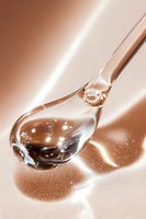 Transparent glass spoon with liquid droplet casting dramatic shadow on rose gold surface, glowing highlights and reflections create luxurious cosmetic mood.