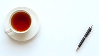 Cup of tea and elegant pen on clean white background for business workspace and office productivity concepts.