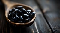 Black beans in wooden spoon on dark rustic table, macro food photography with shallow depth of field and moody lighting, fresh organic legumes.