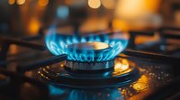 Blue gas flame burning on kitchen stove with warm bokeh background lights. Close up view of natural gas burner ring showing energy consumption and cooking.