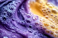 Purple and golden water droplets on smooth surface creating abstract liquid texture with vibrant color gradient and reflective bubbles for modern design.