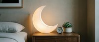 Glowing crescent moon lamp on wooden nightstand creates warm ambient lighting in modern bedroom interior for relaxation and sleep decor.