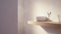 Wooden shelf with rolled towel and lavender sprigs against purple and white wall with natural sunlight for spa and bathroom design.