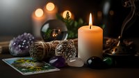 Mystical fortune telling setup with burning candle, crystal ball, sage bundles, amethyst crystals and tarot cards creating atmospheric divination scene.