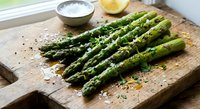 Fresh green asparagus spears seasoned with salt and pepper on rustic wooden cutting board with lemon and herbs for healthy cooking and meal preparation.