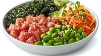 Fresh poke bowl with raw tuna chunks, edamame beans, shredded carrots, seaweed and sesame seeds served in white ceramic bowl on white background.