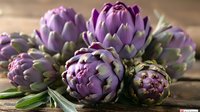 Fresh purple artichokes with green leaves on rustic wooden background, perfect for food blogs, restaurant menus and healthy eating lifestyle content, macro photography.