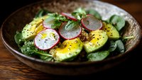 Fresh avocado salad with sliced radishes and mixed greens in rustic bowl, healthy vegetarian meal with herbs and black pepper seasoning.