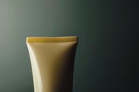 Minimalist composition of cream tube container with gold cap against dark green background, highlighting product packaging design and cosmetic industry.