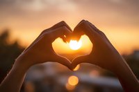 Hands forming heart shape silhouette against golden sunset sky with warm bokeh lights creating romantic atmosphere for love and connection concepts.