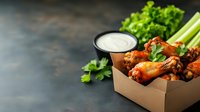 Spicy buffalo chicken wings served in eco-friendly takeout box with celery sticks, ranch dipping sauce and fresh herbs on dark background. For food delivery menu.