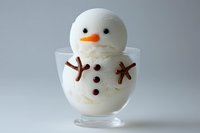 Vanilla ice cream shaped like a snowman in glass bowl with chocolate stick arms and candy features, perfect for winter dessert menus.