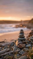 Balanced stone cairn on rocky beach at golden hour sunset with soft waves and warm sky creating peaceful meditation and mindfulness atmosphere.