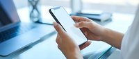 Professional woman using smartphone with blank white screen at modern office desk for mobile app mockup and digital communication.