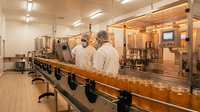 Two male technicians in white lab coats working at modern pharmaceutical production line with glass bottles on conveyor belt in sterile manufacturing facility.