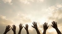 Silhouettes of diverse hands raised up against dramatic cloudy sky background expressing unity, hope, volunteering and community support concept.