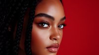 Young African American woman with braided hair and flawless makeup against red background, showcasing professional beauty and cosmetic artistry in dramatic lighting.