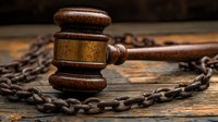 Wooden judge gavel surrounded by rusty metal chain on aged wooden surface in dramatic lighting, symbolizing law enforcement and justice system concepts.
