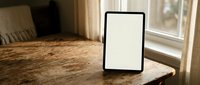 Digital tablet with blank white screen on rustic wooden table near window in cozy home interior for mockup presentations and app development.