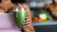 Young African American woman holding fresh green smoothie with manicured nails. Healthy lifestyle and wellness concept showing detox drink in kitchen setting.