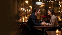 Young couple enjoying romantic dinner date with red roses in elegant restaurant with warm lighting and festive atmosphere for Valentine's Day celebration.