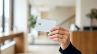 Woman holding blank white credit card in modern home interior with natural light and contemporary furniture.